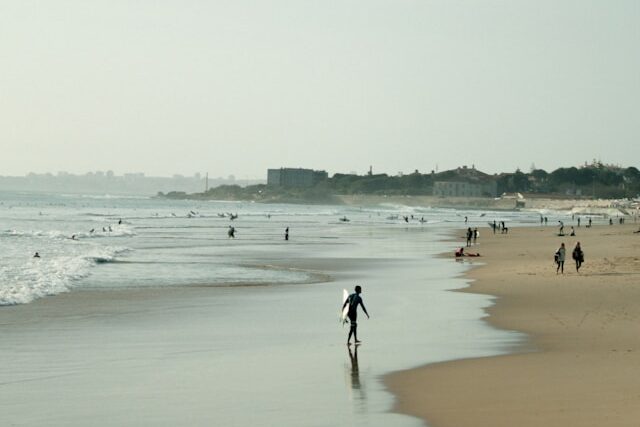 Surfers walking along Praia de Carcavelos beach with boards in hand