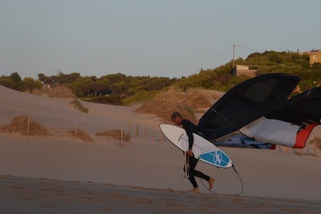 Surfer walking up the sandy dunes of Praia do Guincho with board in hand,