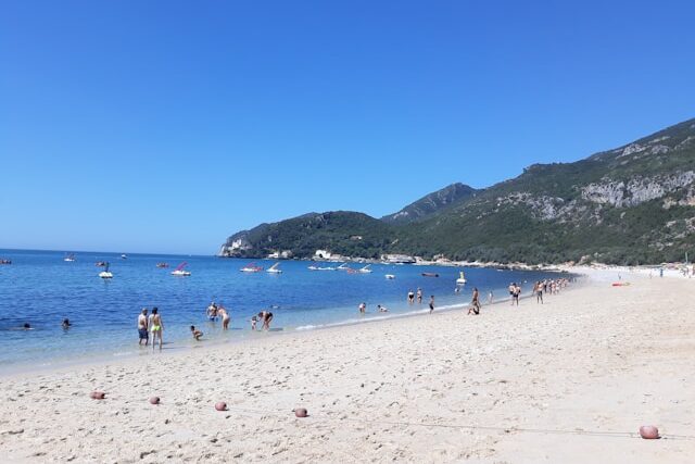 People on a sandy beach in Setubal surrounded by green montains