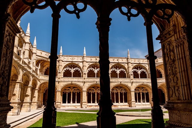 Green courtyard at Lisbon Jeronimos Monastery seen through stone arch window