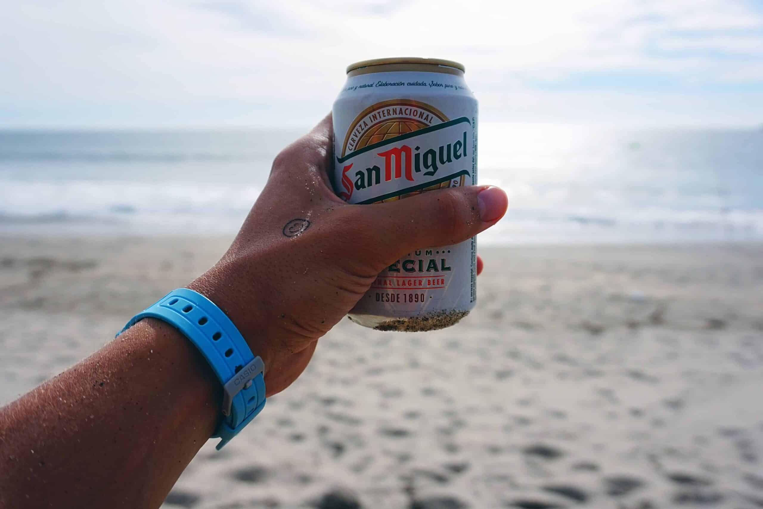 Hand holding a can of San Miguel beer at the beach during a Lisbon stag weekend